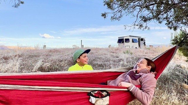 Enfant et adulte dans un hamac rouge avec la roulotte en arrière-plan